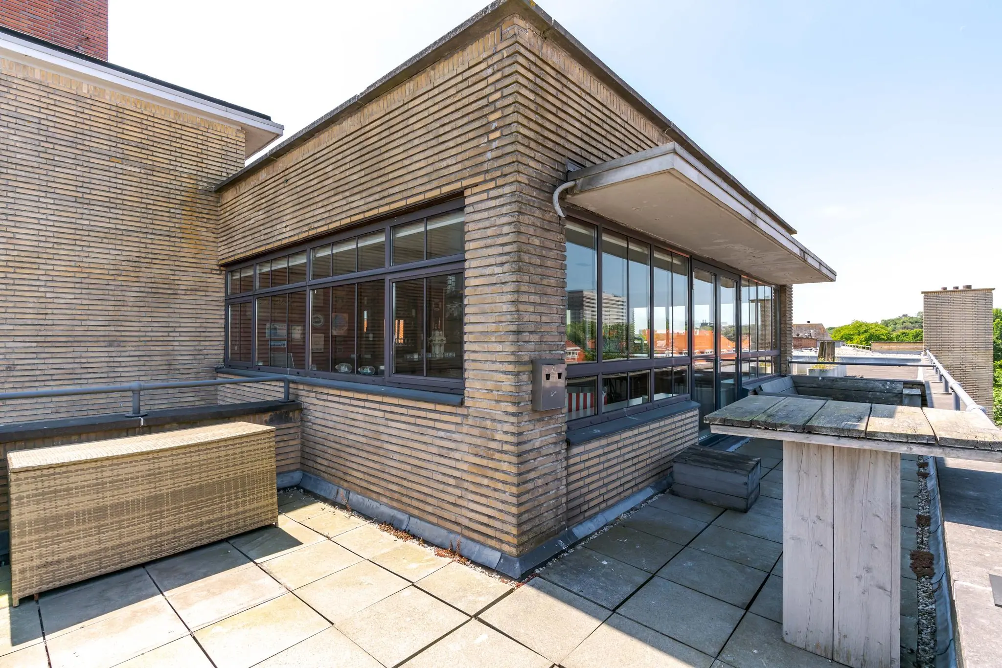 Dakterras met grijze tegels en uitzicht op de Van Alkemadelaan, grenzend aan een hoekwoning met grote ramen.